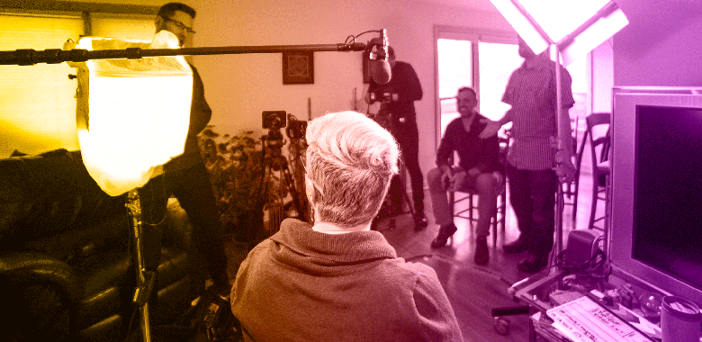 Over-the-shoulder shot of a female patient preparing to be interviewed in a living room while the Brella Productions video crew sets up around her.