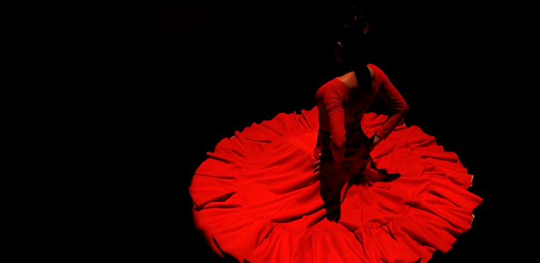 A female dancer in flowing red dress poses on a dark stage