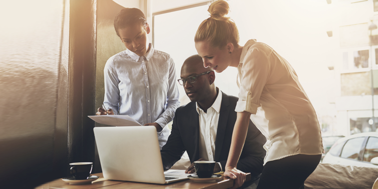 Three young business professionals look at laptop screen in café.