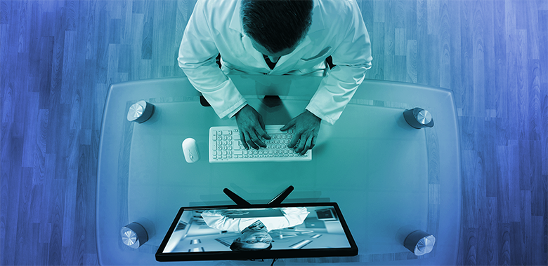 Overhead shot of male doctor in a lab coat working at a desktop computer.