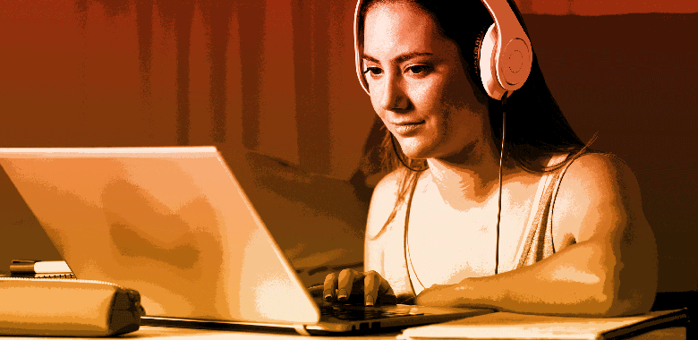 A female student wearing headphones watches a video on laptop.