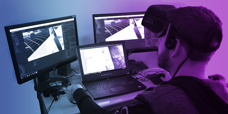 A Brella Productions developer sits at a desk wearing a VR headset, working on a virtual reality experience at a computer workstation.