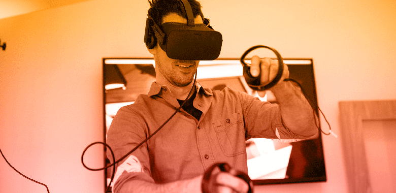 A man wearing a VR headset uses hand controllers to play a VR game at a Brella-hosted event.