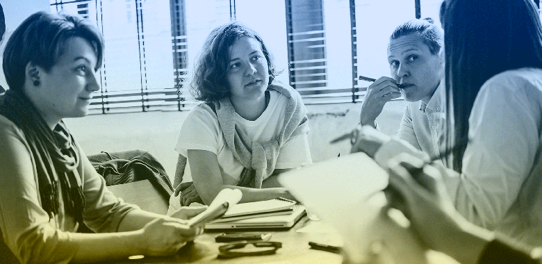 Four women sit around a table engaged in discussion at table.