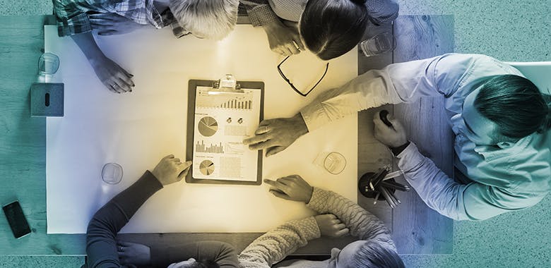 Overhead shot of five professionals sitting at a table reviewing data.