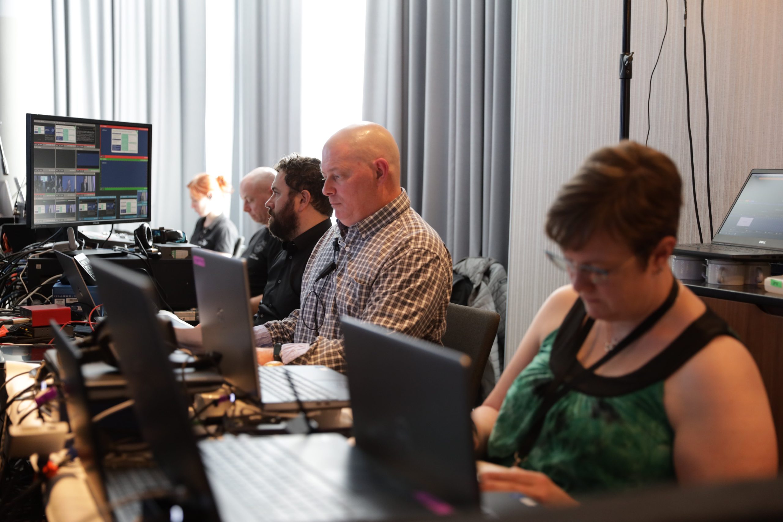 A male Brella producer, two male and two female Brella event technicians working on laptops with supplemental monitors at a corporate event.