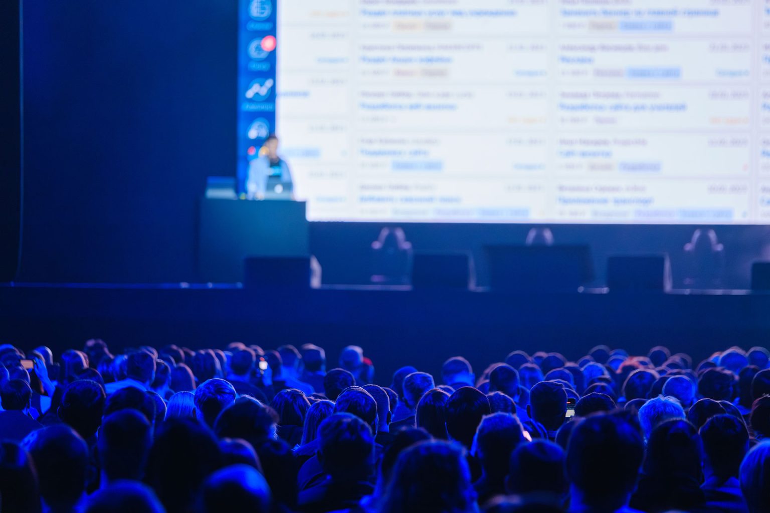 Business crowd attending global presentation in blue-lite auditorium.
